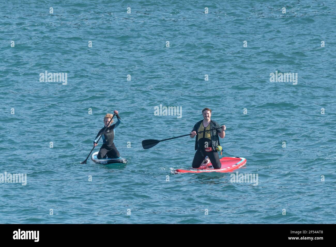 Two holidaymakers kneeling on Stand Up Paddleboards in Newquay Bay in Cornwall. Stock Photo