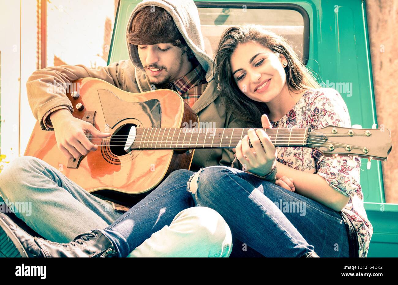 Romantic couple of lovers playing guitar on old fashioned mini car - Nostalgic retro concept of love with soft focus on the faces of boyfriend and gir Stock Photo