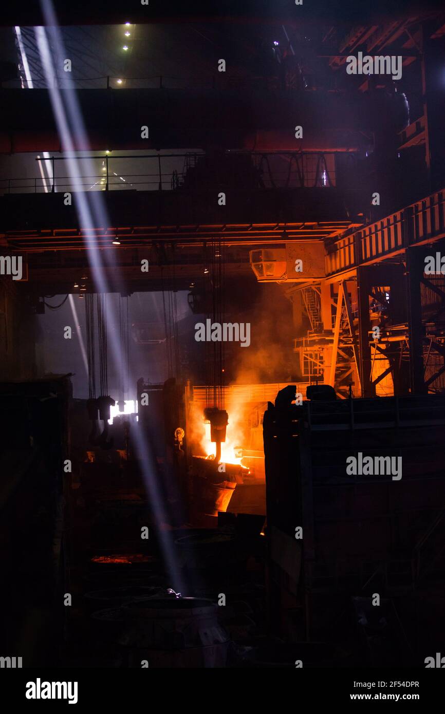 Metal alloy plant. Metallurgical bucket with liquid hot metal. Overhead crane and ray of daylight. Stock Photo
