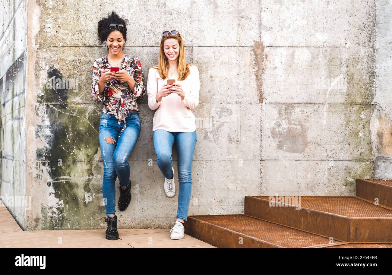 Happy girls best friends having fun outdoors with mobile smart phone - Friendship concept with millenial girlfriends on smartphones Stock Photo