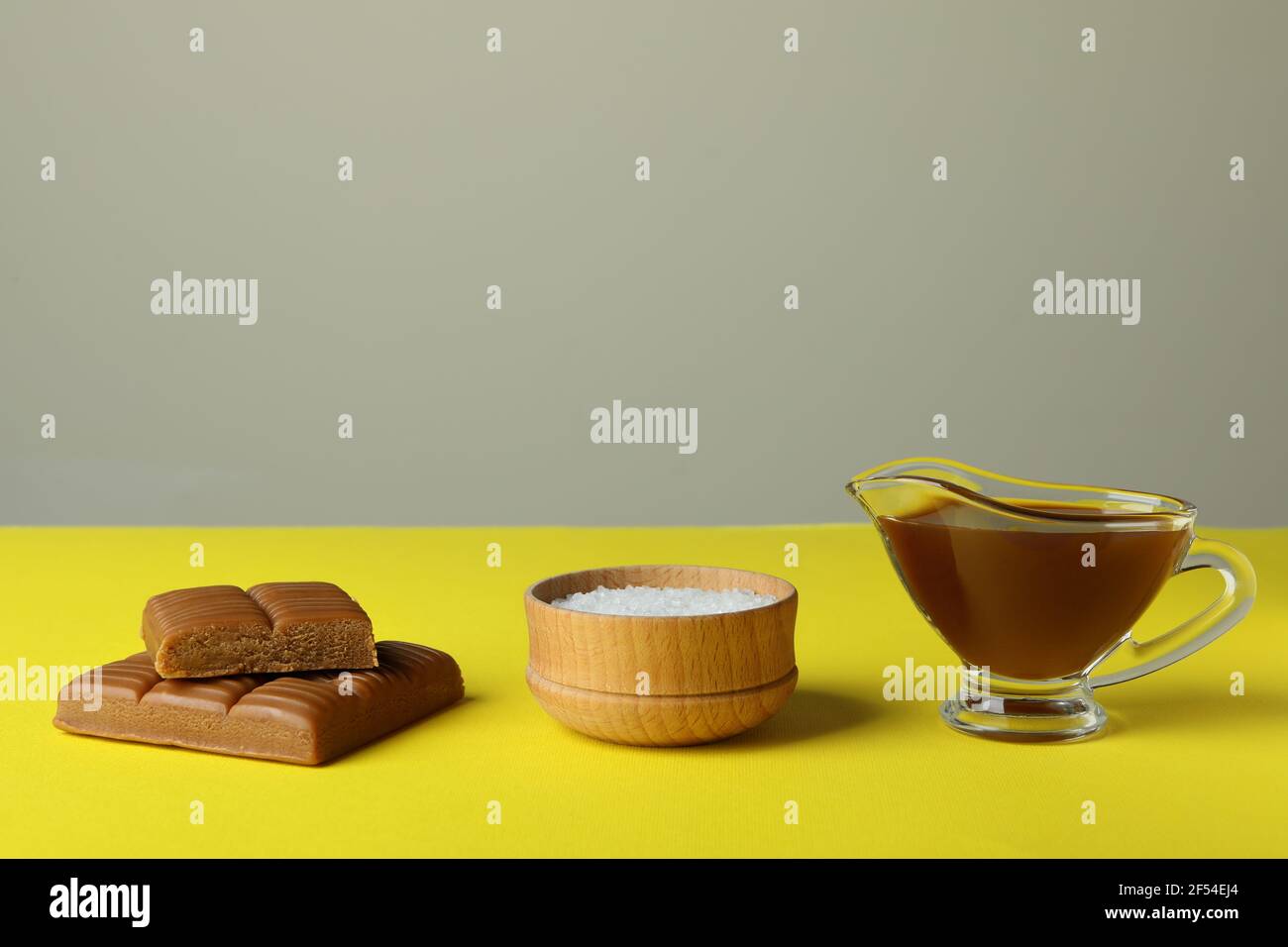 Caramel pieces, sauce and bowl of salt on yellow table Stock Photo