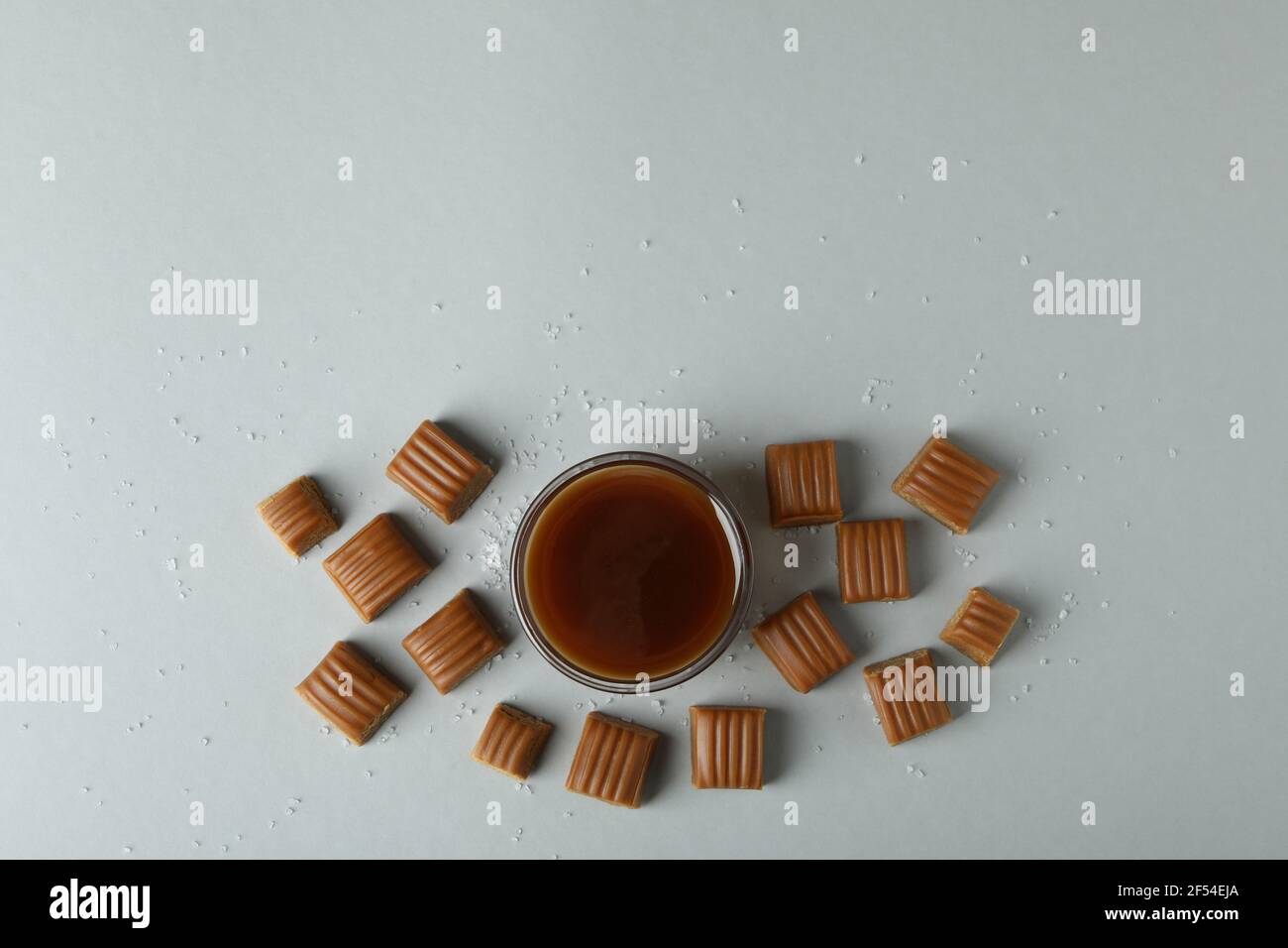 Salted caramel pieces and bowl of sauce on light gray background Stock Photo