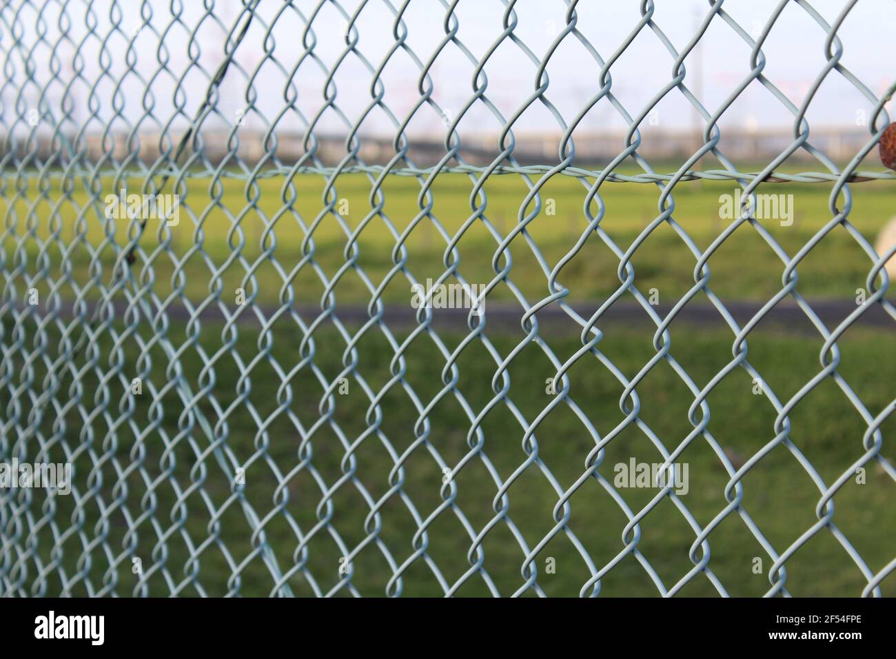 metallic mesh with green field behind, metal fence Stock Photo - Alamy