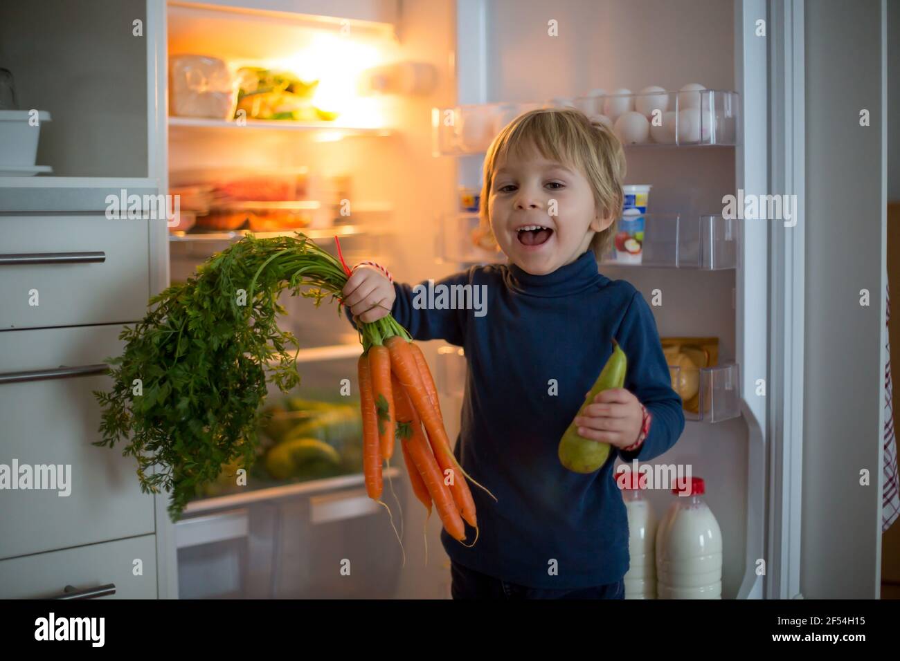 Cute toddler blond child, opening the fridge door and taking fruits adn