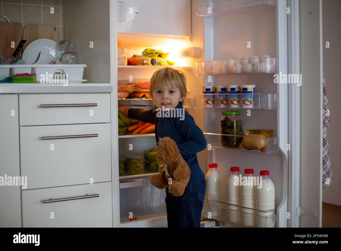 Cute toddler blond child, opening the fridge door and taking fruits adn