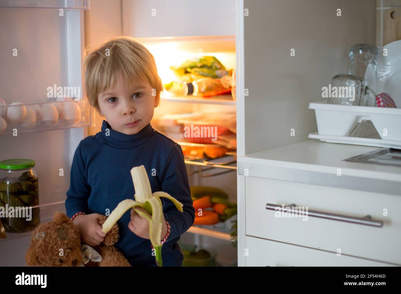 Cute toddler blond child, opening the fridge door and taking fruits adn