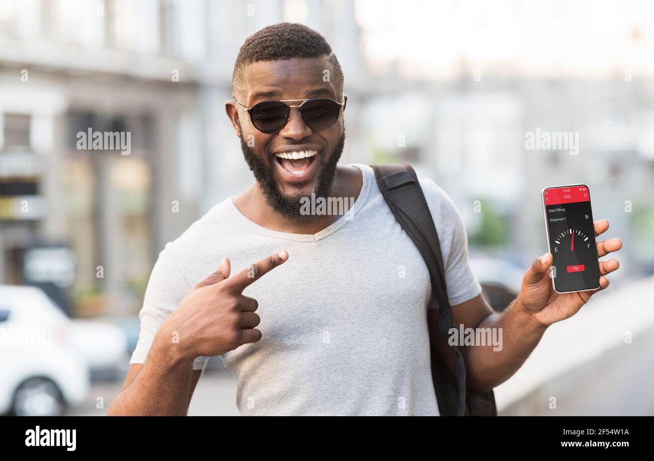 Online smart payment technology. Black guy pointing at smartphone with mobile app for contactless fuel purchase outdoor Stock Photo