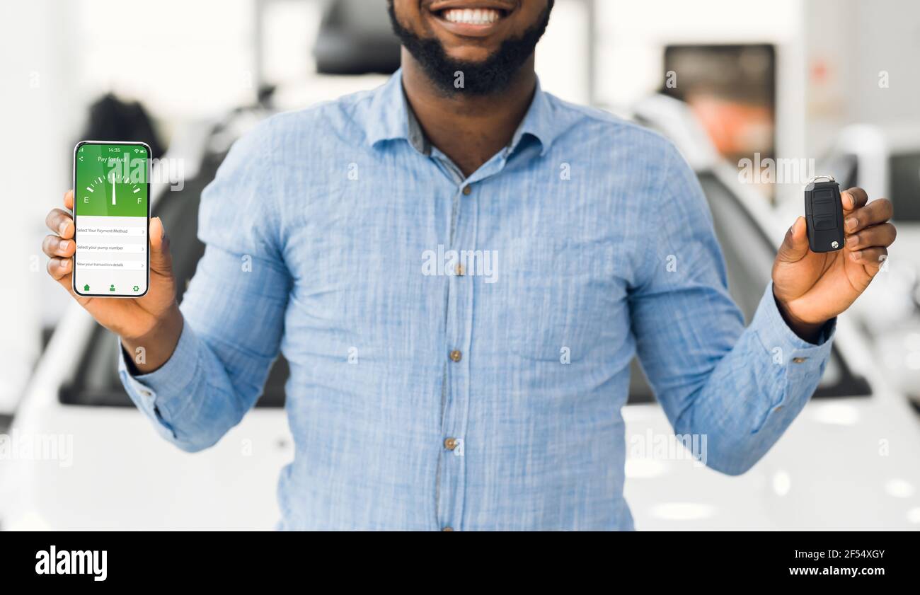 Cropped view of happy black guy holding car key and smartphone with online fuel shopping app on screen, outdoors Stock Photo