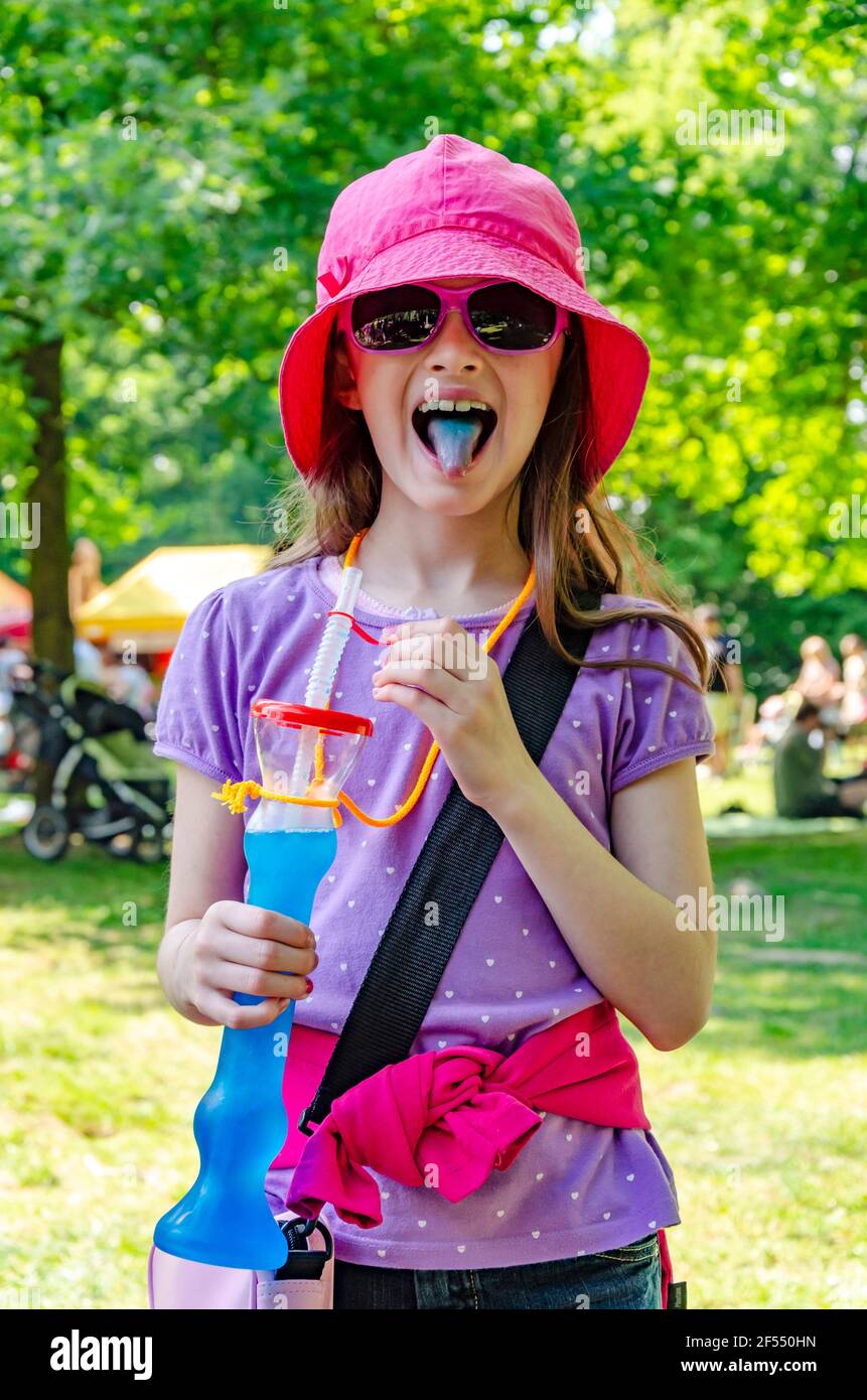 Smiling young girl with open mouth, blue tongue out, holding in her hand a fake plastic hookah with blue lemonade and a straw Stock Photo