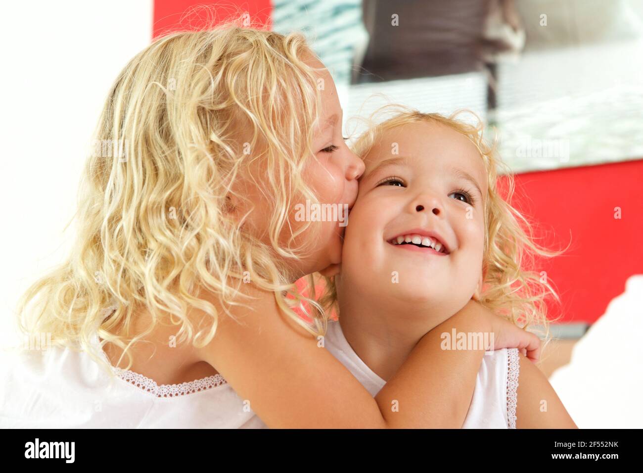Close up portrait of cute little girl kissing her sister on bed at home Stock Photo