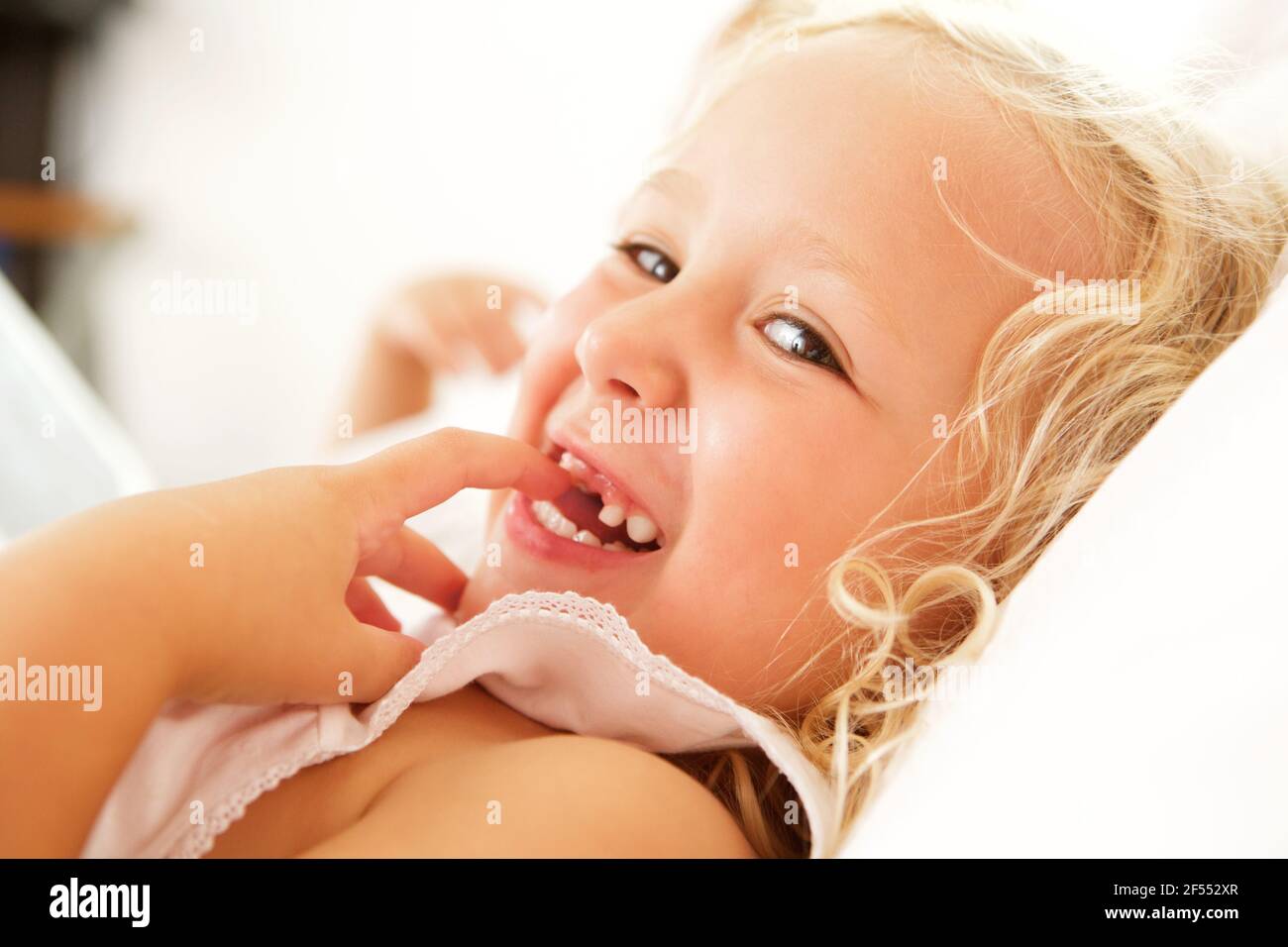 Close up portrait of beautiful little girl lying on bed and smiling Stock Photo