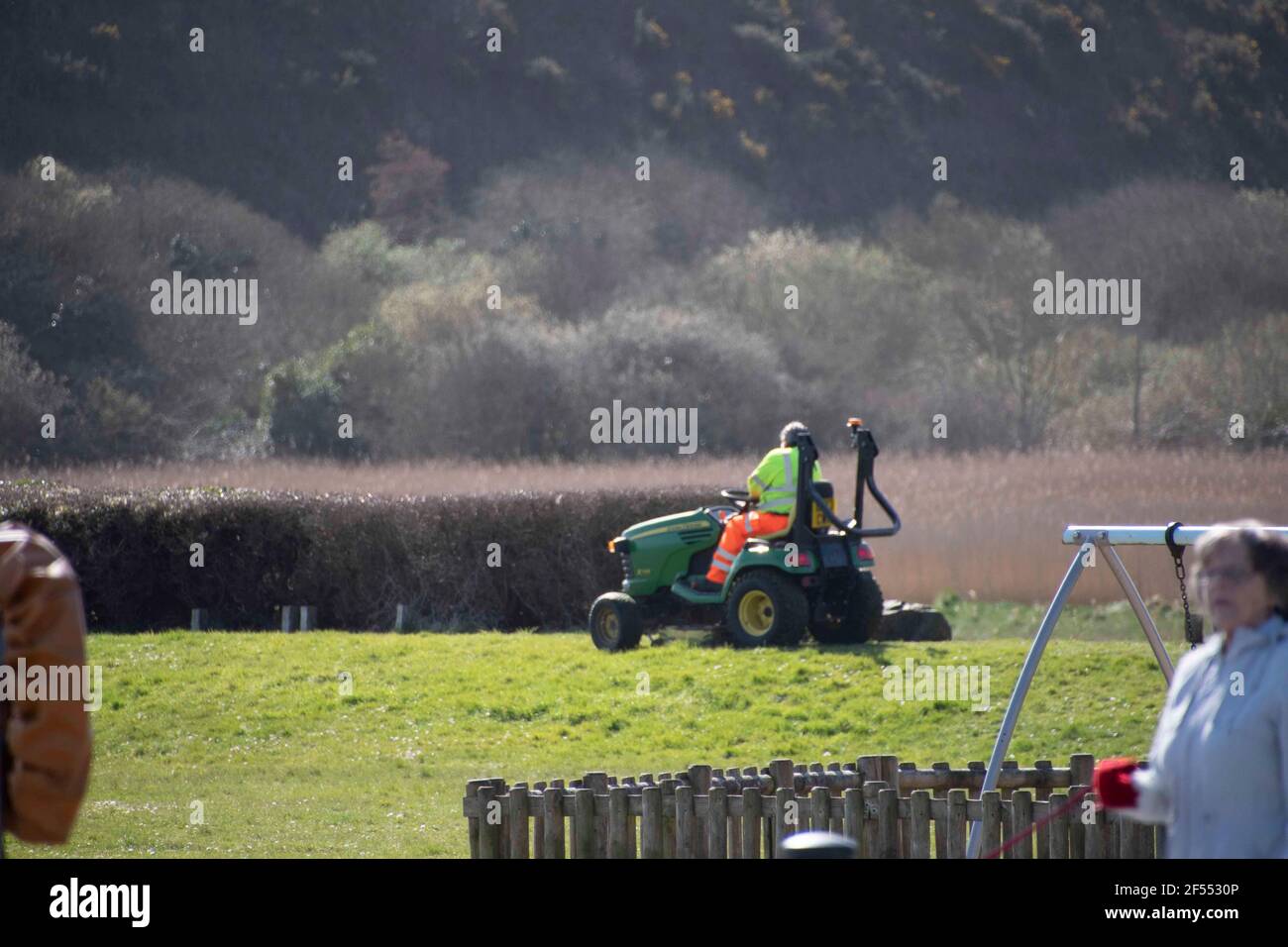 Fishguard, Pembrokeshire, uk .24 March  2021. Workers in their  high vis jackets ride  on grass cutters  as  more visitors  arrive ,Pembrokeshire County Council therefore has a difficult  to strike a balance as some cutting is essential for safety purposes, yet it is very keen to see al wild wildlife thrive wherever possible.  . Credit: Debra Angel/Alamy Live News Stock Photo