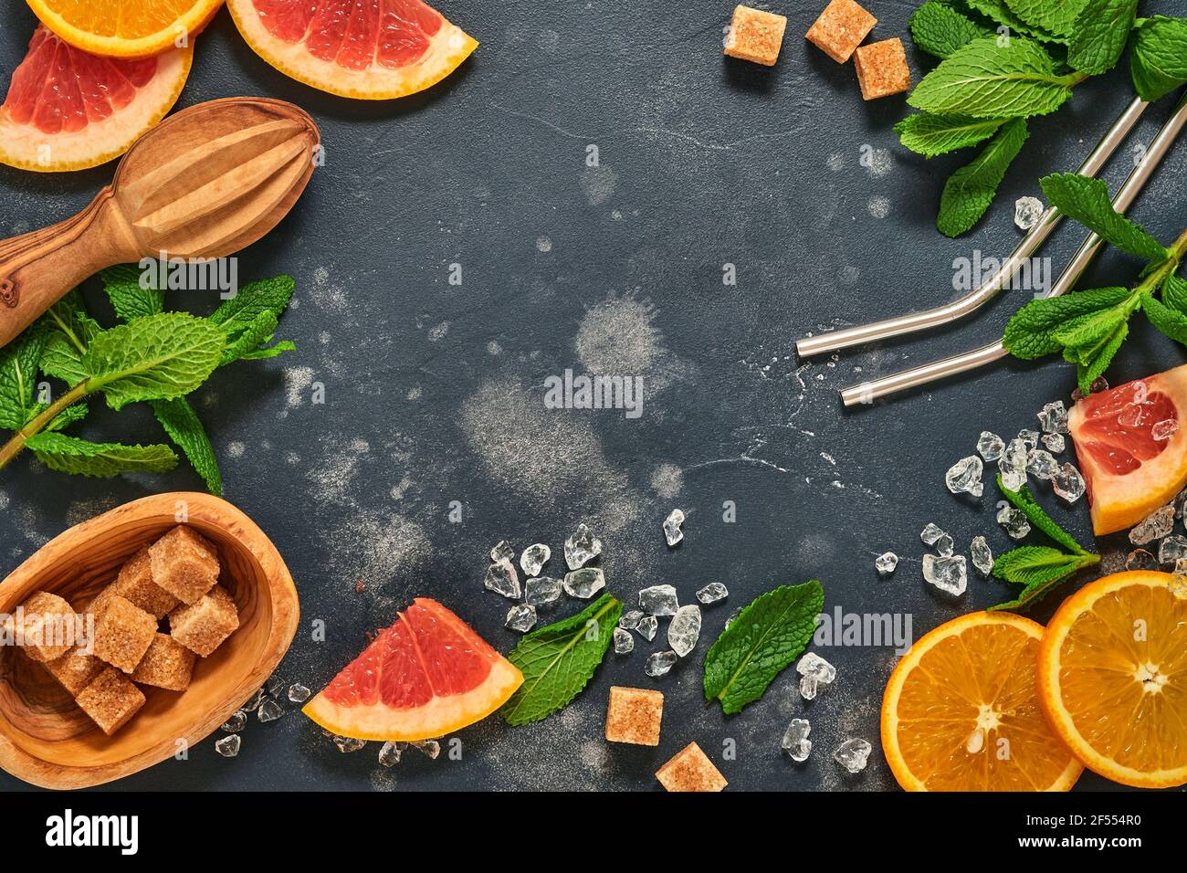 Grapefruit and orange slices, mint, cane sugar, ice, cocktail tubes, juicer or squeezer on black stone old background. Ingredients for making summer b Stock Photo