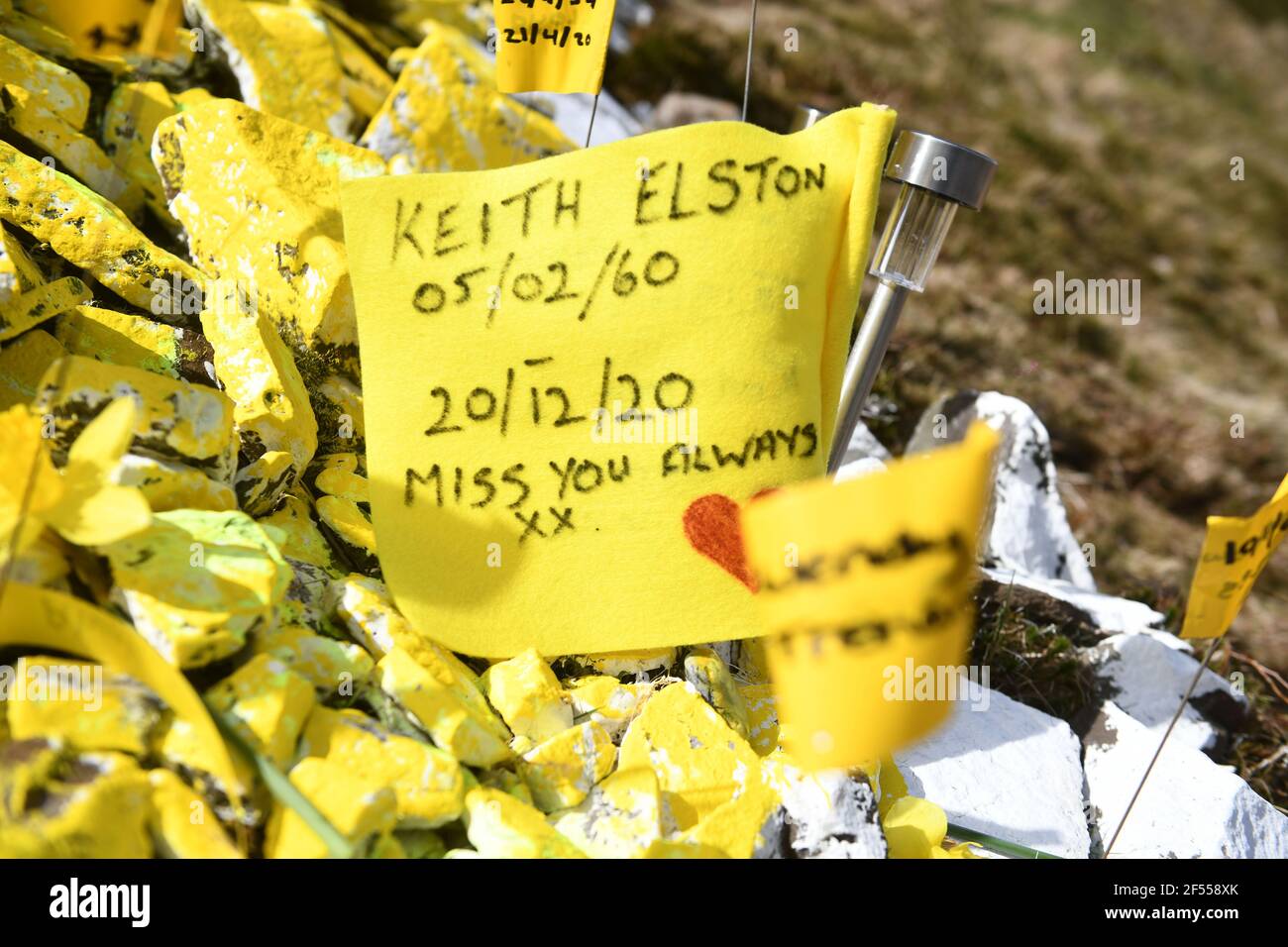 The yellow heart on the Bwlch mountain in the Rhondda Valley, which has become a tribute for famines across Wales who have lost loved ones to Coronavirus. The heart, which is made up of stones, is covered with flags carrying the names of victims and personal messages. Stock Photo