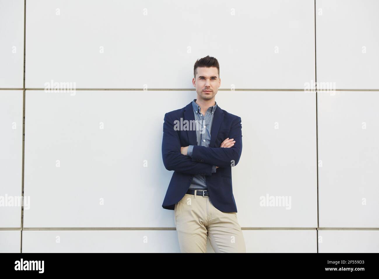 Portrait of young business man standing against white wall with arms ...