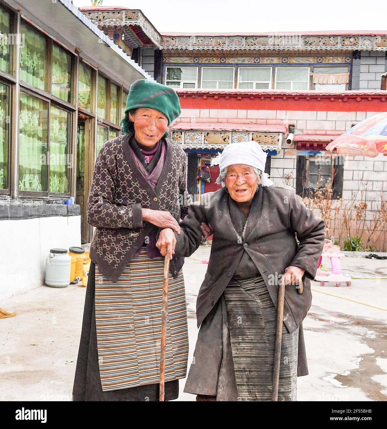 (210324) -- LHASA, March 24, 2021 (Xinhua) -- Drolkar (R) poses for a photo with her daughter in front of their house in Qugaqiang Village of Lhunzhub County, Lhasa, southwest China's Tibet Autonomous Region, March 22, 2021. Drolkar, born in 1927, is a villager in Qugaqiang Village of Lhunzhub County, Lhasa. In old Tibet, Drolkar had to go to Lhasa to carry stones for building. 'Every time, the serf owner would stamp my forehead and arms as proof. Sometimes my forehead and arms were full of seals after work,' Drolkar said. 'We were told to sing while working at the construction site. Wh Stock Photo