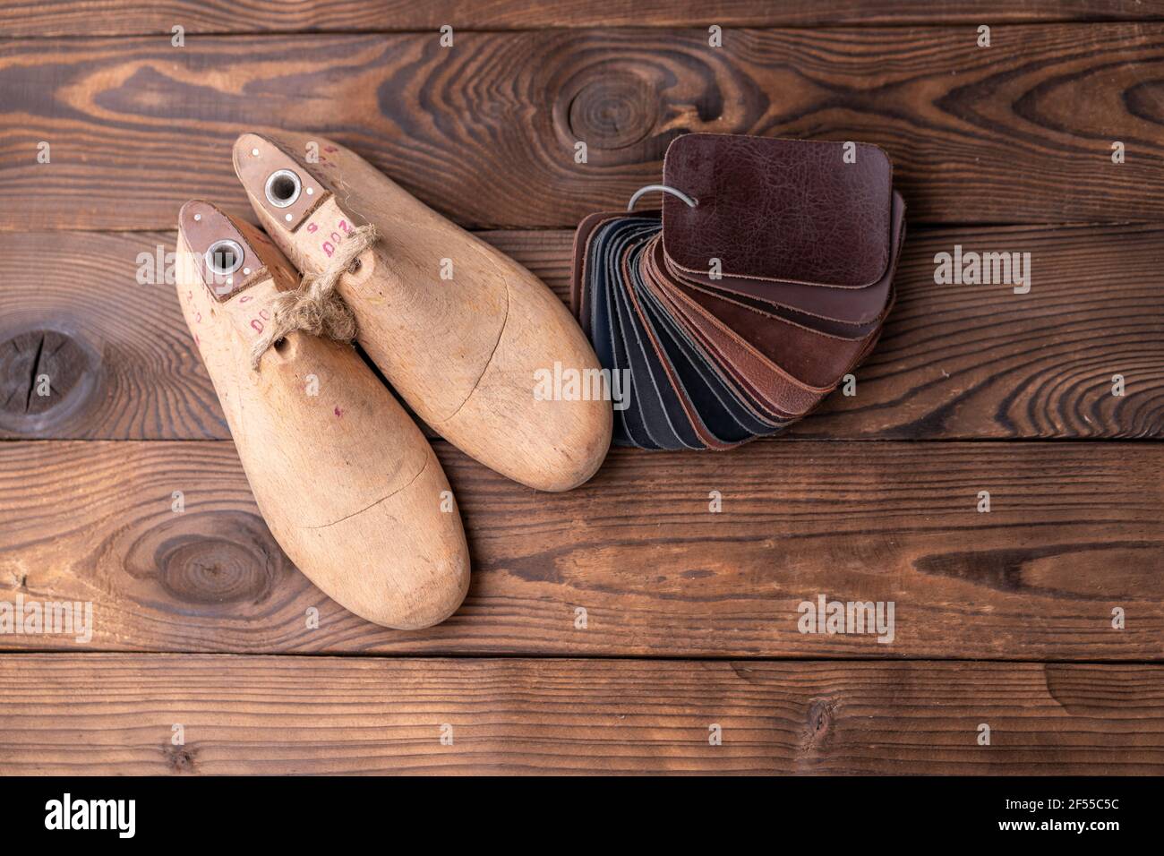 Leather samples for shoes and wooden shoe last on dark wooden table. Designer furniture clothes. Shoe maker workspace. Stock Photo