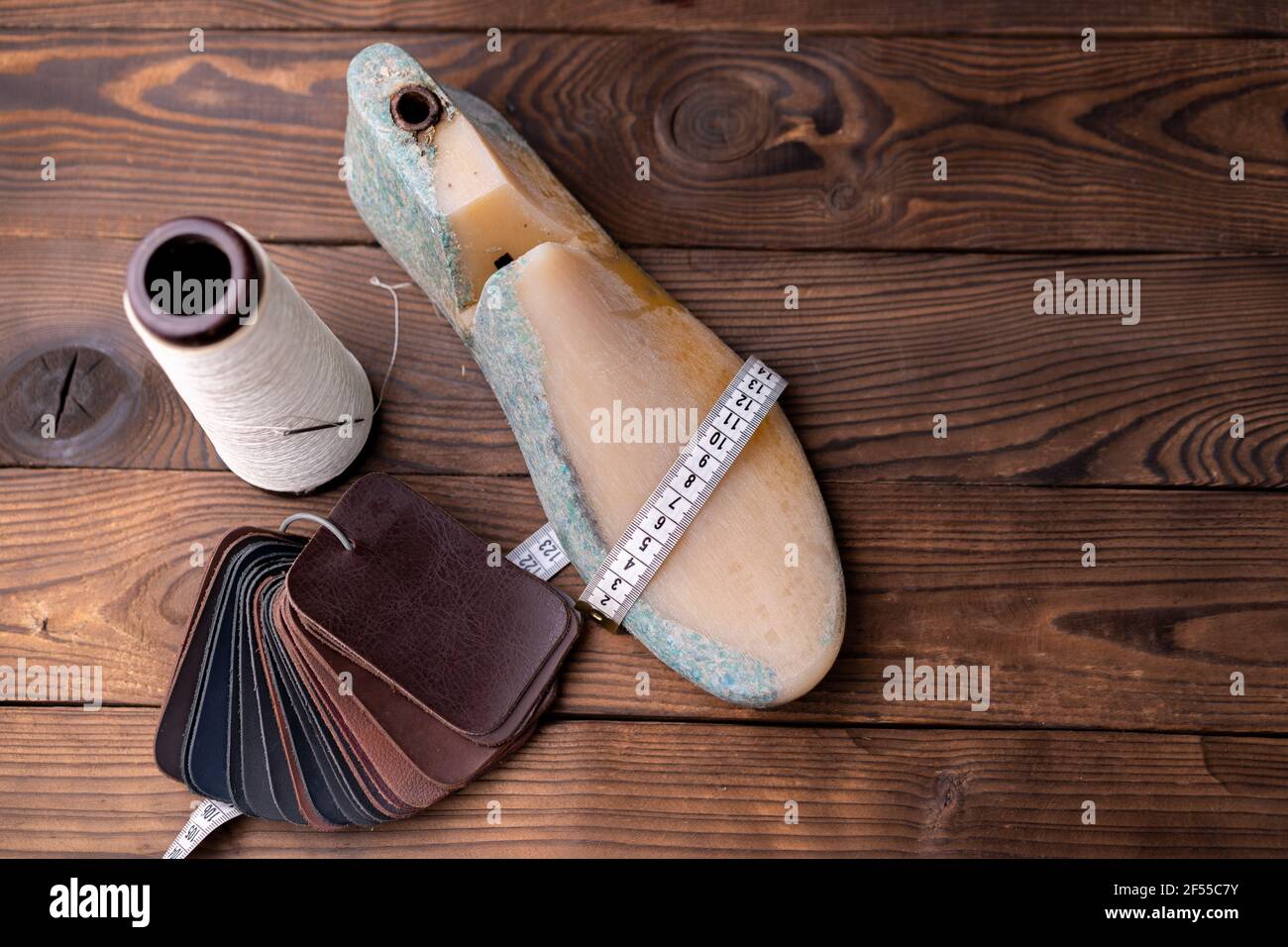 Leather samples for shoes and wooden shoe last on dark wooden table. Designer furniture clothes. Shoe maker workspace. Stock Photo