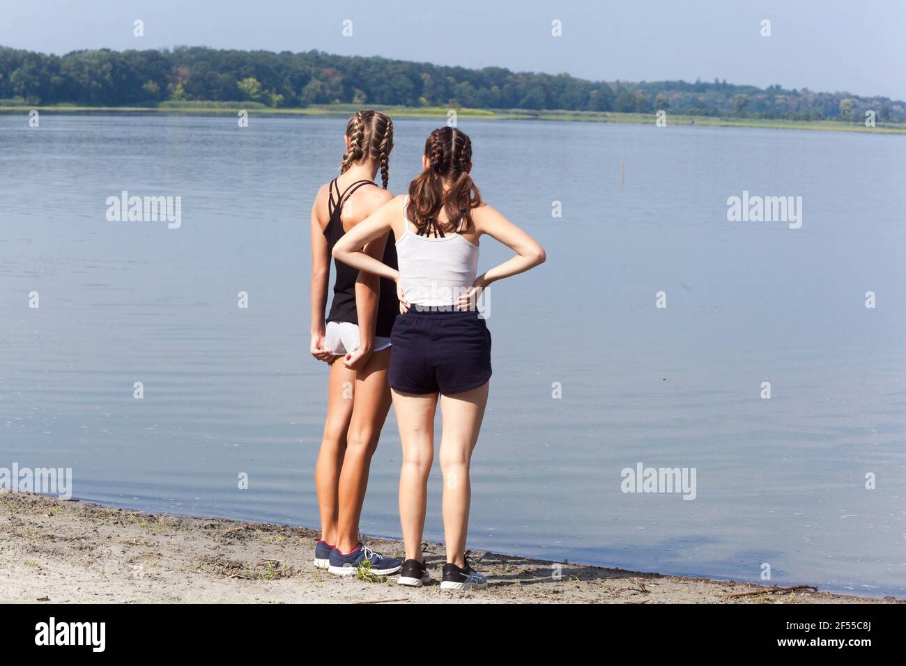 Two teenage girls on shore pond, rear view Stock Photo