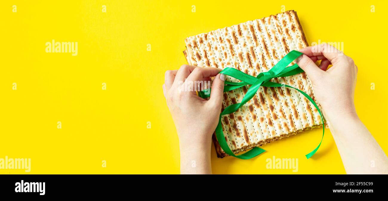 Hands hold matzo bread on yellow background. Happy Passover. Celebration of Jewish religious holiday Pesach. Copy space. Stock Photo
