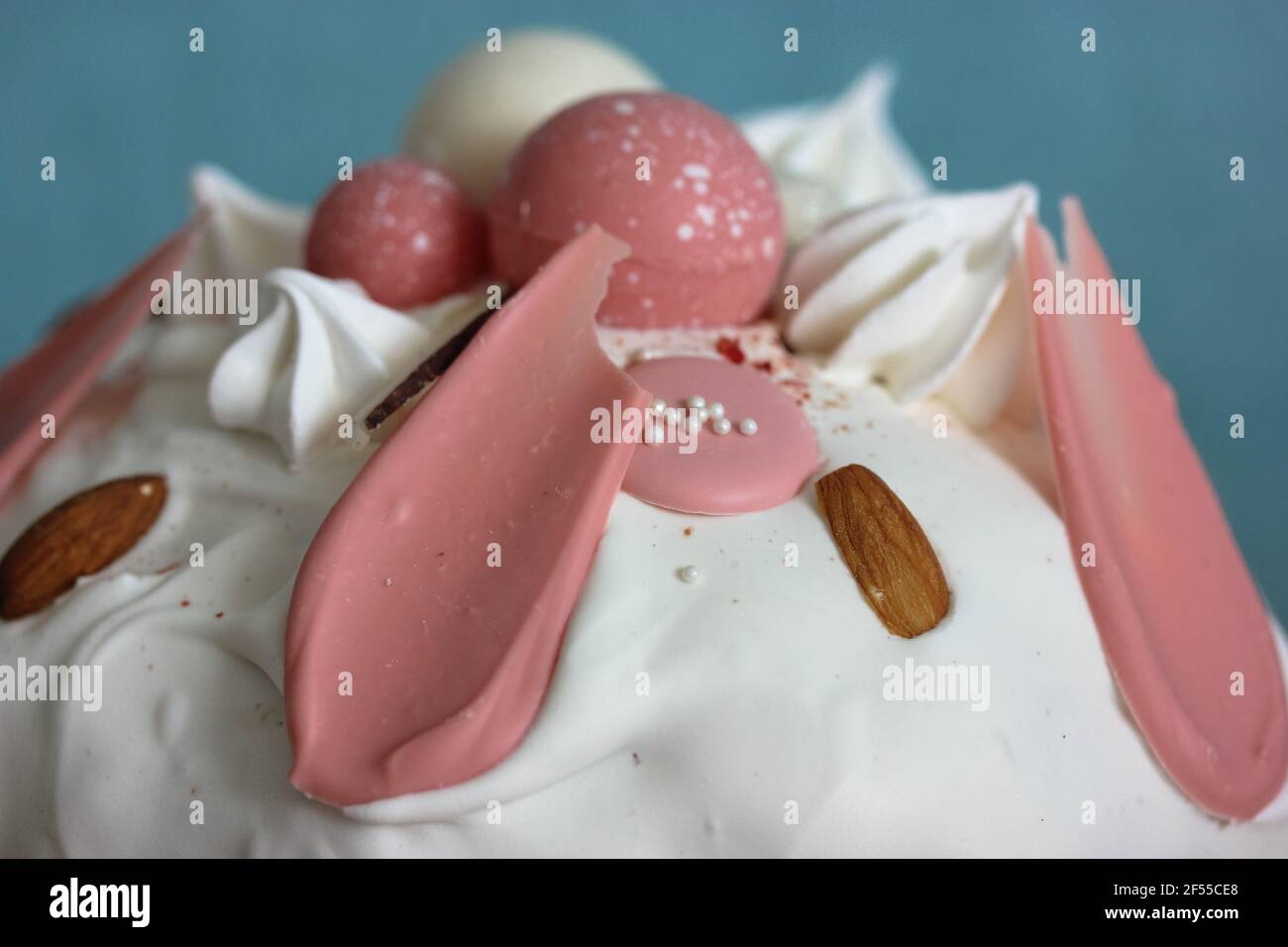 Easter cake decorated with white icing, meringue, pink decorative chocolate balls, nuts. Homemade Easter bread top view on blue background. A recipe f Stock Photo