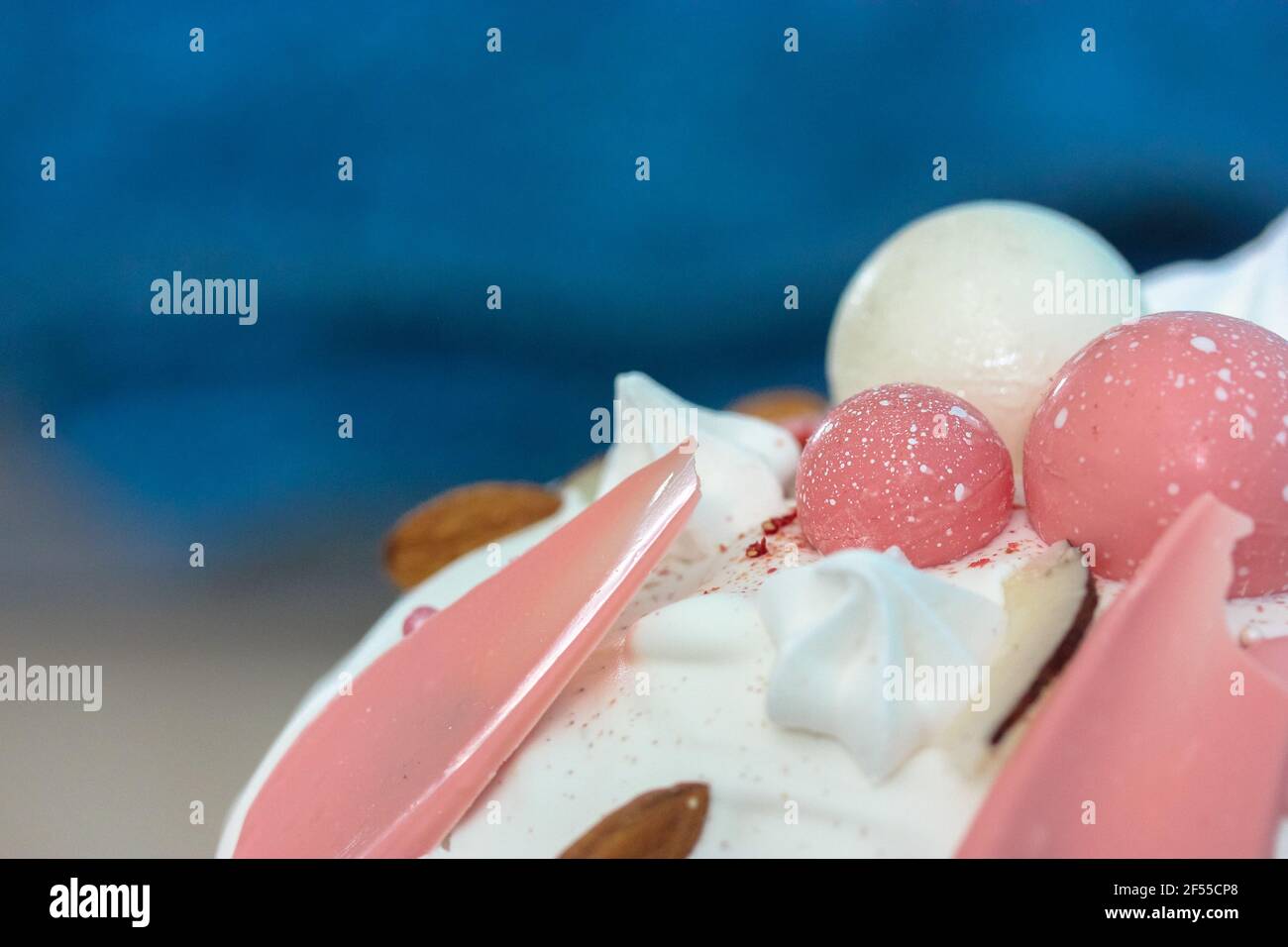 Easter cake decorated with white icing, meringue, pink decorative chocolate balls, nuts. Homemade Easter bread top view on blue background. A recipe f Stock Photo