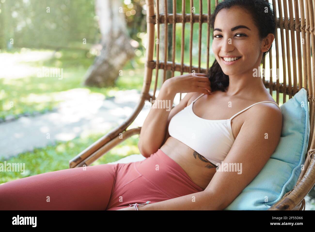 Woman feeling energized and upbeat after morning yoga exercises in garden.  Attractive smiling female in sports bra, leggings lying rattan armchair  Stock Photo - Alamy