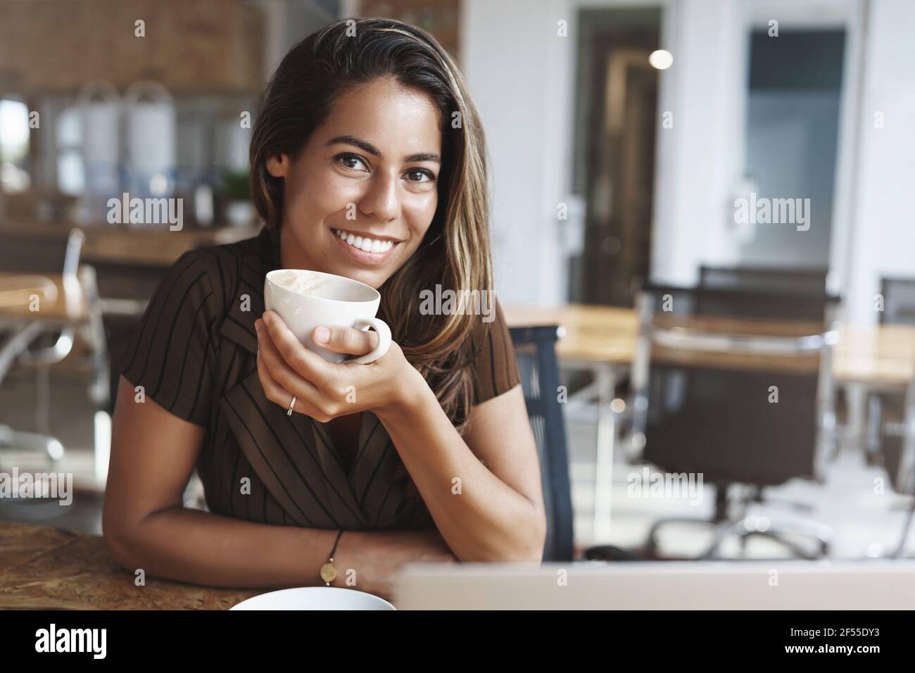 Wellbeing, success, happiness concept. Adorable smiling happy young tanned woman pierced nose hold coffee cup grinning joyfully camera sit cafe table Stock Photo