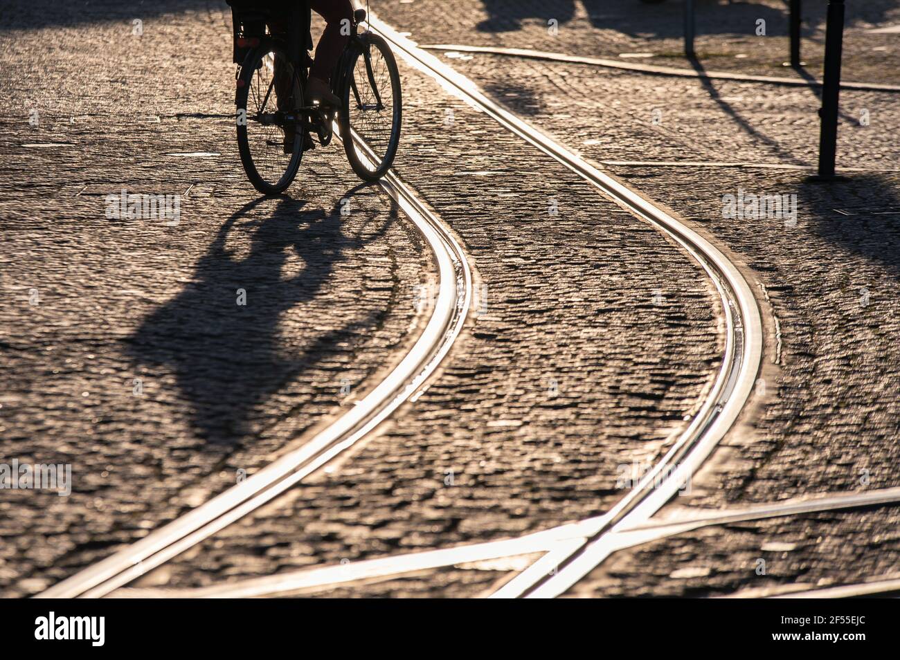City life depicted with a cyclist in the sunrise on a cobblestone street with tram rails Stock Photo