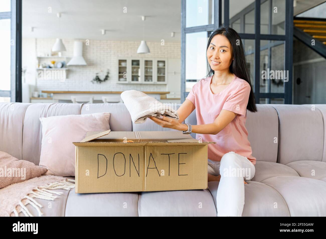 Darkhaired young Asian woman sitting on the couch at home and