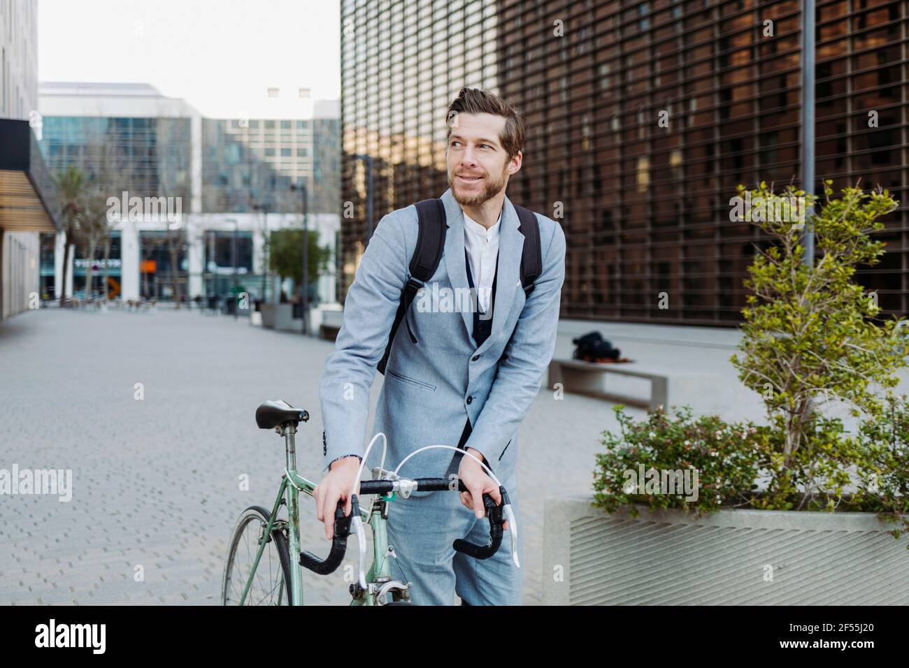 Male commuter wearing back pack walking with bicycle on road in city Stock Photo