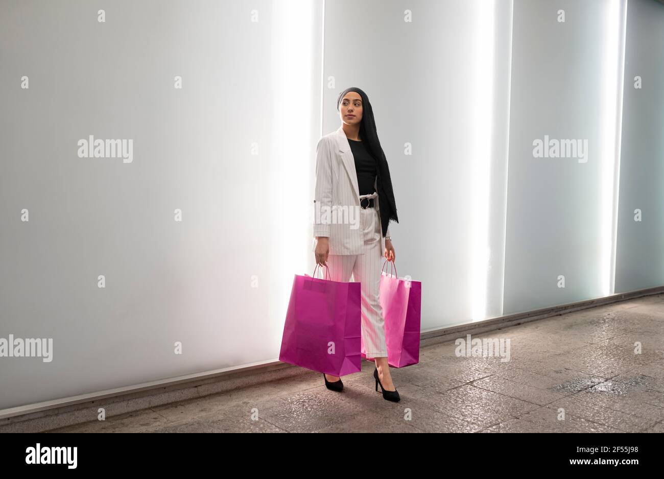 Beautiful Arab woman looking away while holding bags in shopping mall Stock Photo