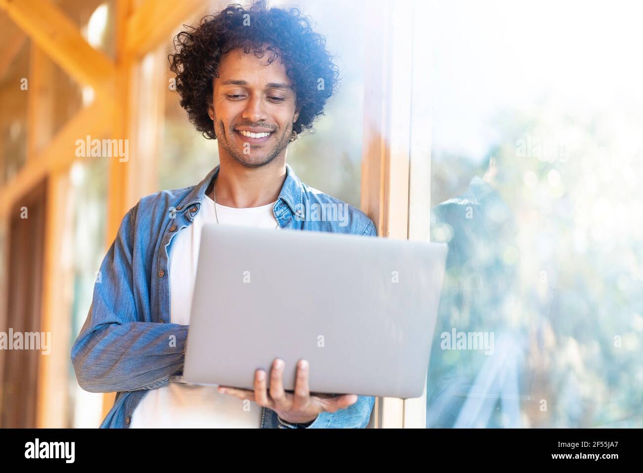 Smiling man using laptop while standing by front yard window Stock Photo