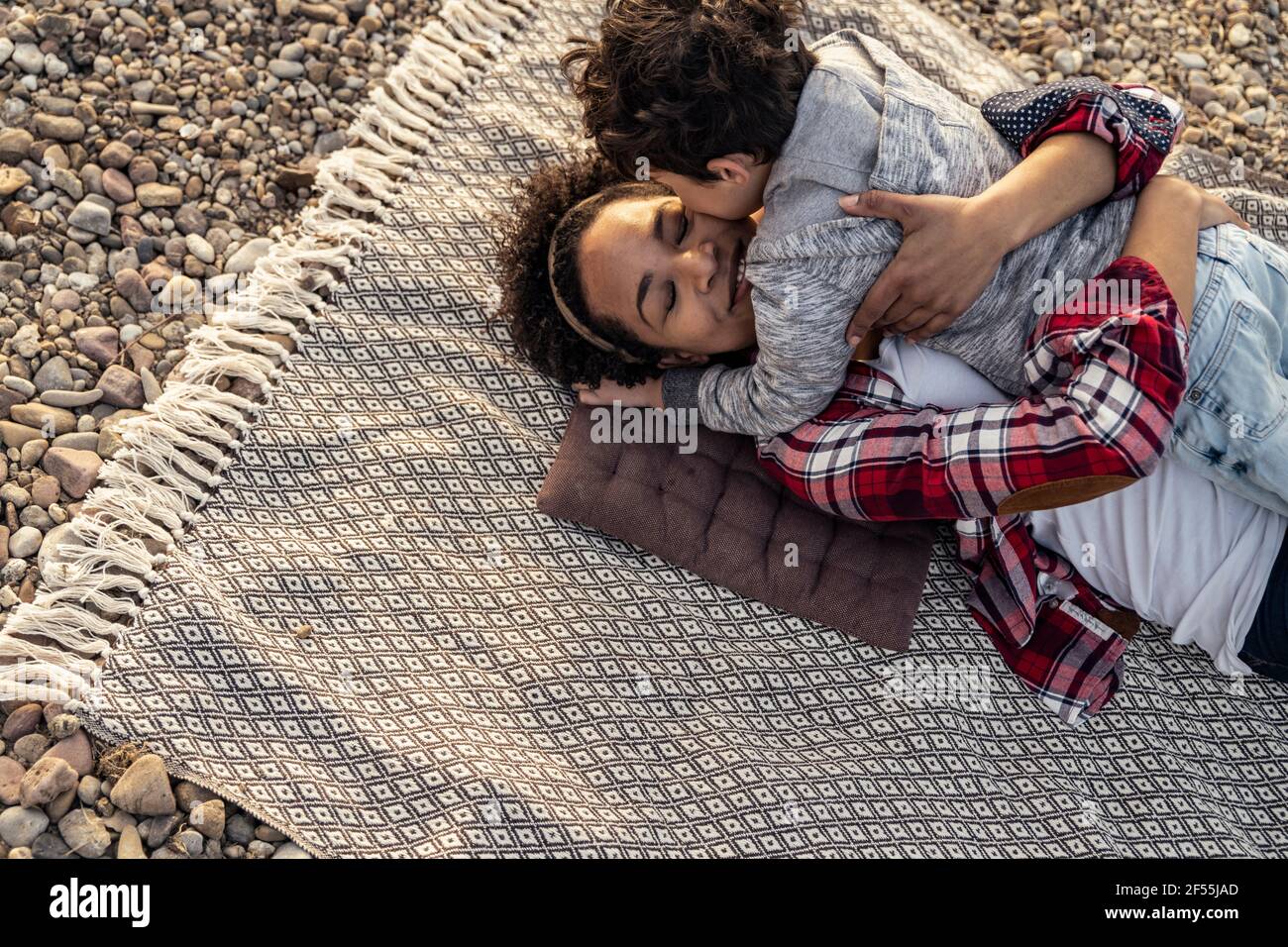 Woman embracing boy while lying on blanket over pebble Stock Photo