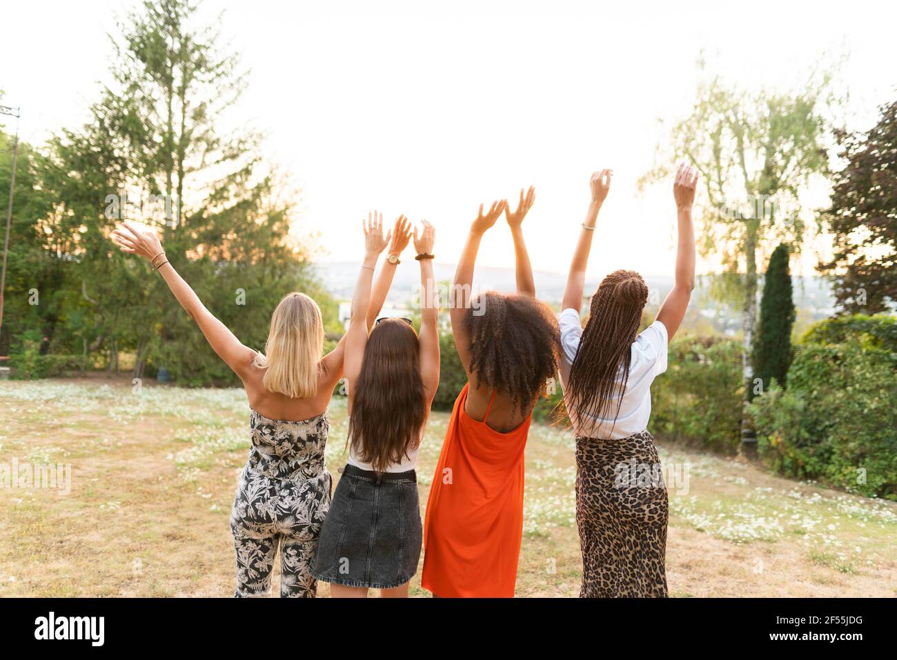 Multi-ethnic female friends standing with hands raised in park Stock Photo