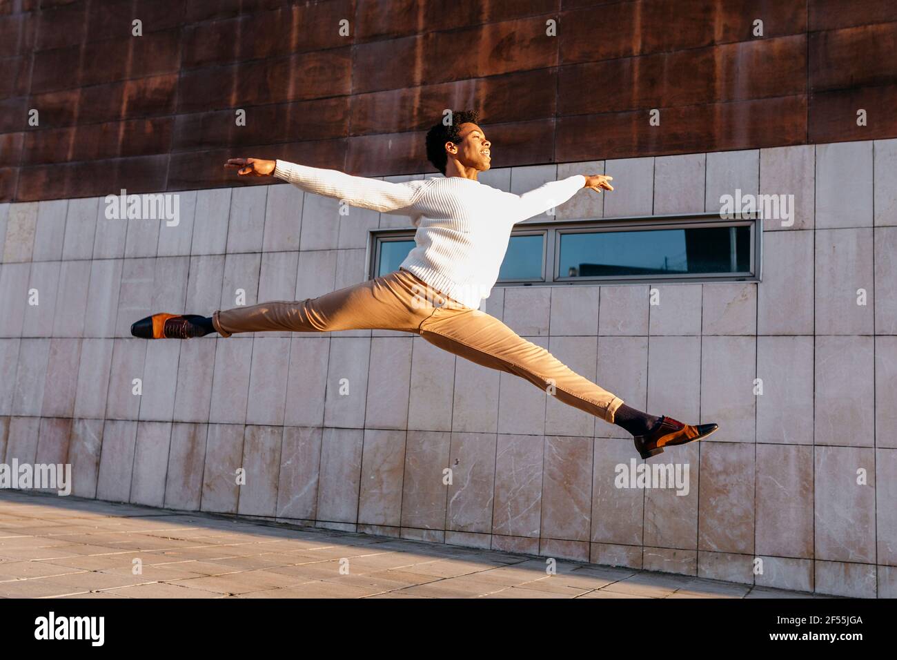 Happy male dancer doing grand jeté against building Stock Photo