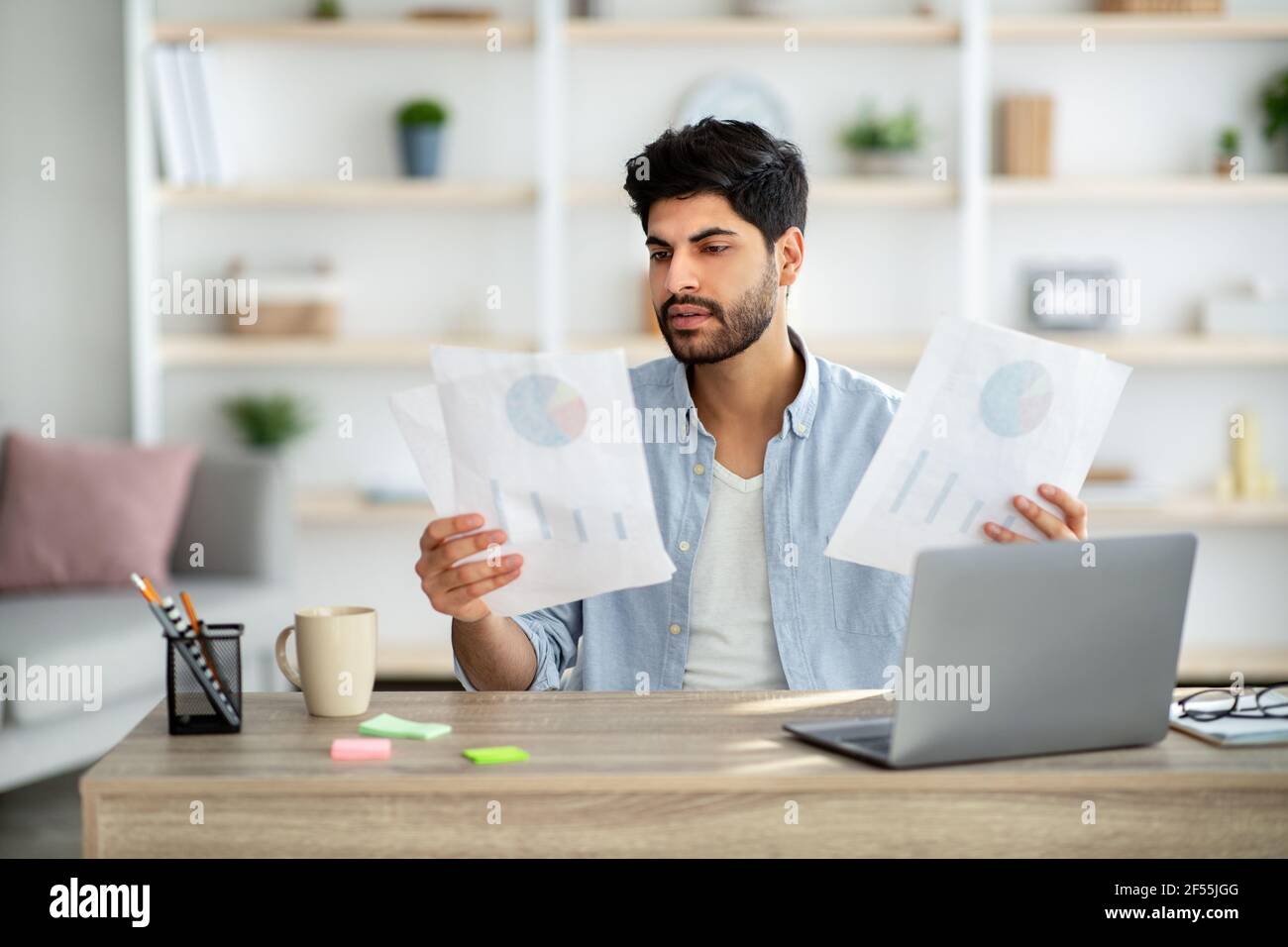Concentrated arab entrepreneur working with financial documents, checking annual reports and using laptop at home Stock Photo