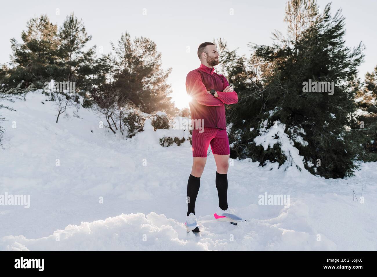 Sportsman with arms crossed standing on snow covered land against clear sky Stock Photo