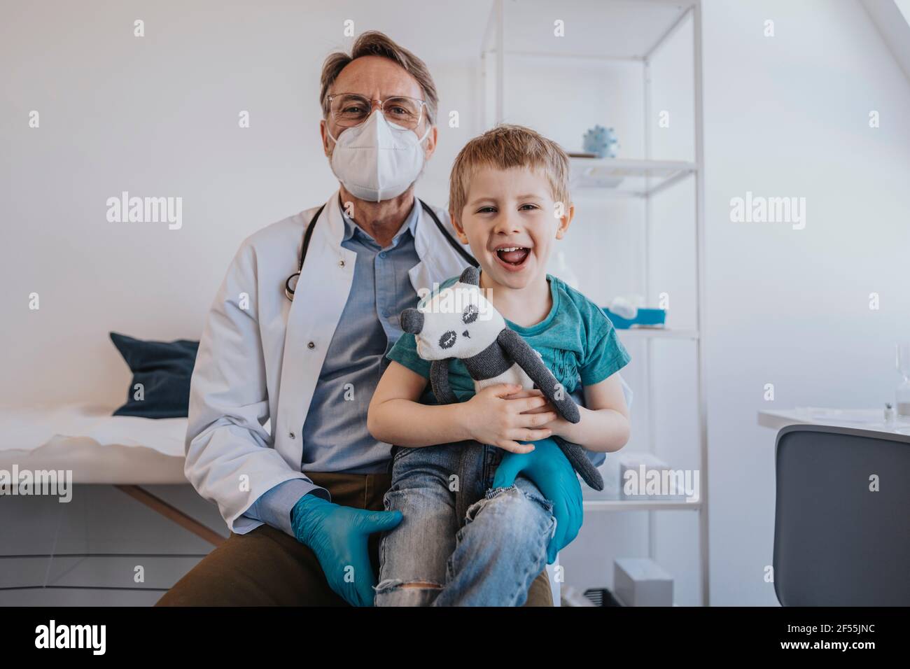 Cheerful boy laughing while sitting on doctor's lap at medical examination room Stock Photo