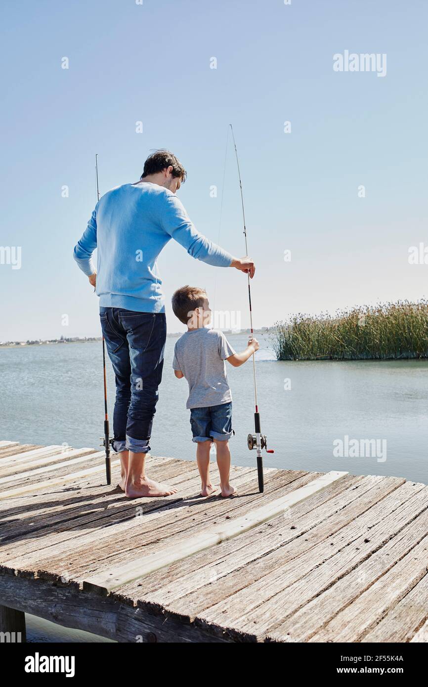 Father and son holding fishing rod while standing on pier Stock