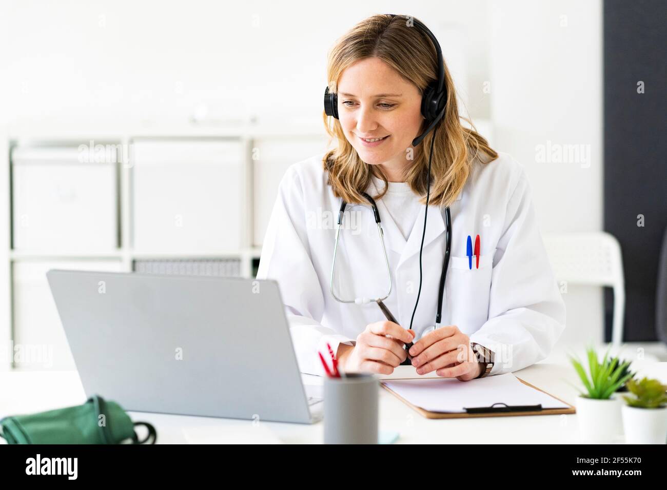 Blond female doctor giving online consultation on laptop in medical clinic Stock Photo