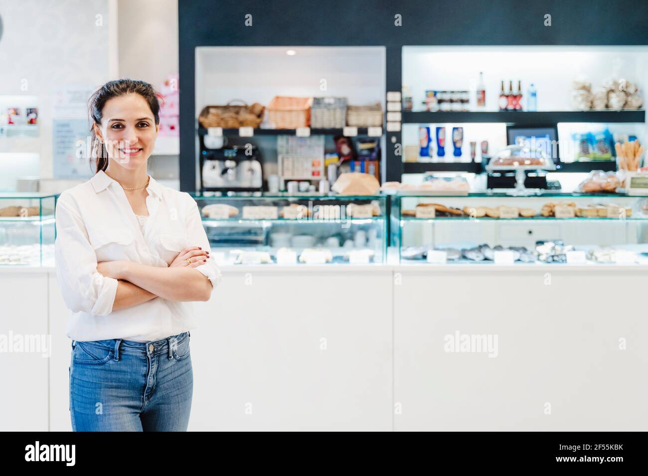 Female bakery owner standing arms crossed against display case Stock Photo