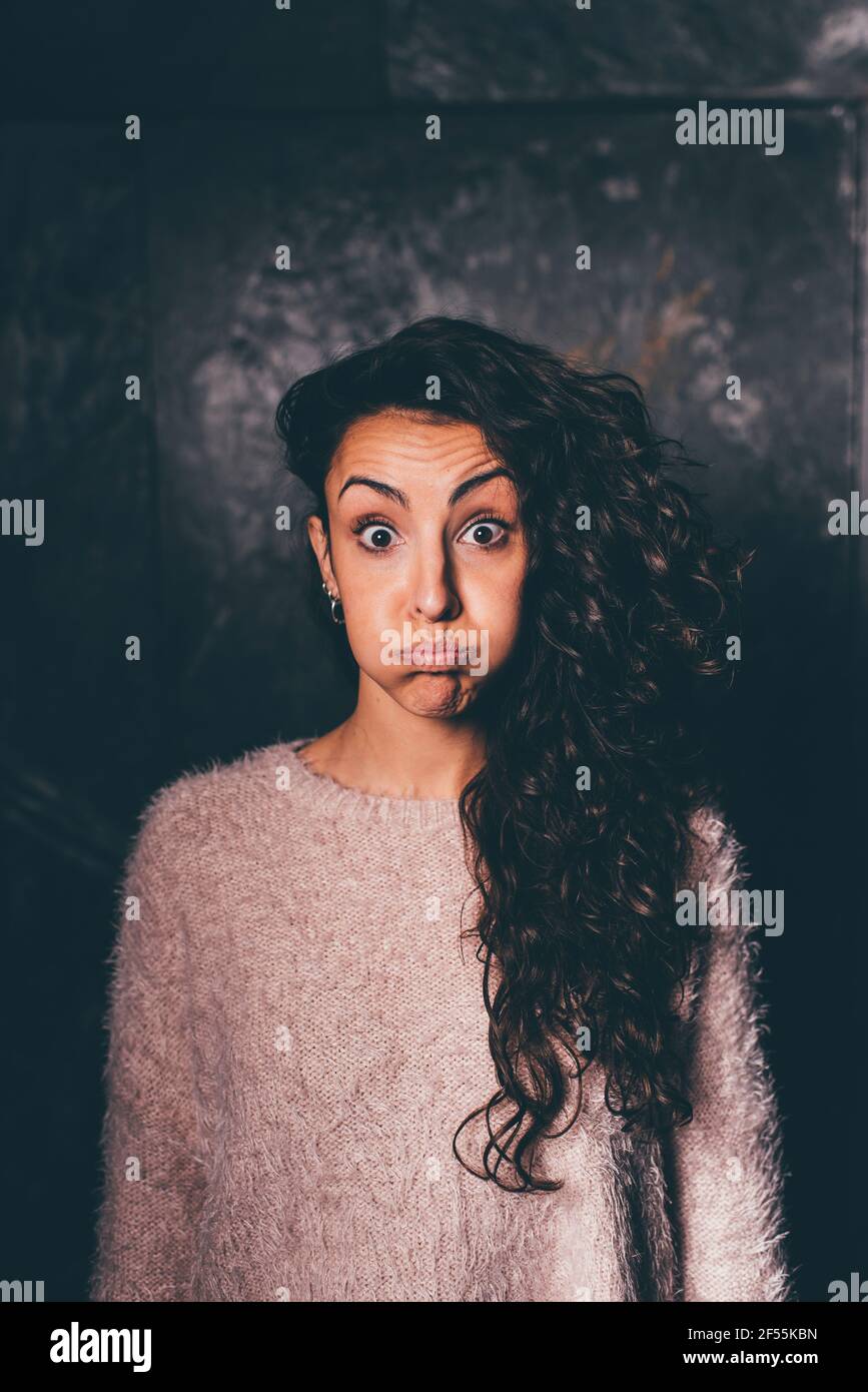 Young woman with long hair making face while standing against wall ...