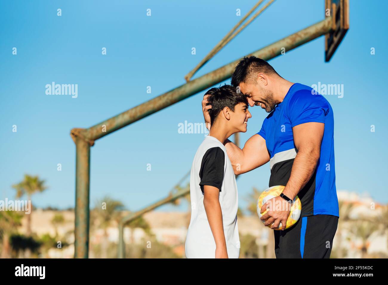 Smiling father and son touching forehead while standing at sports court ...