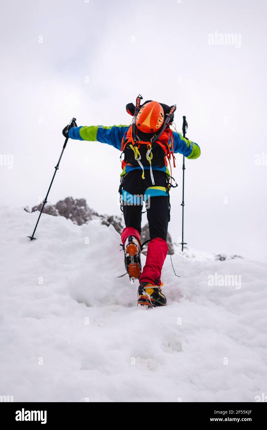 Trekker climbing snowcapped mountain with crampons and hiking poles Stock Photo