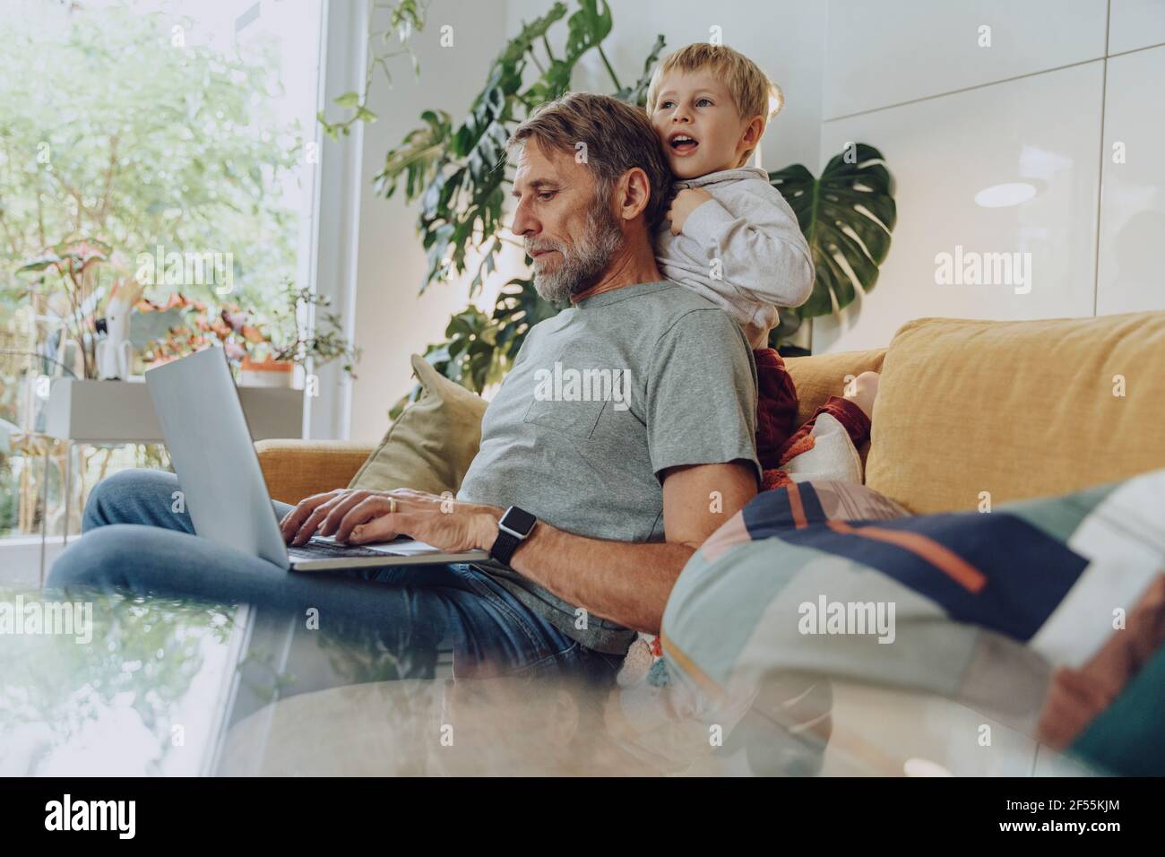 Playful boy leaning on father using laptop at home Stock Photo - Alamy