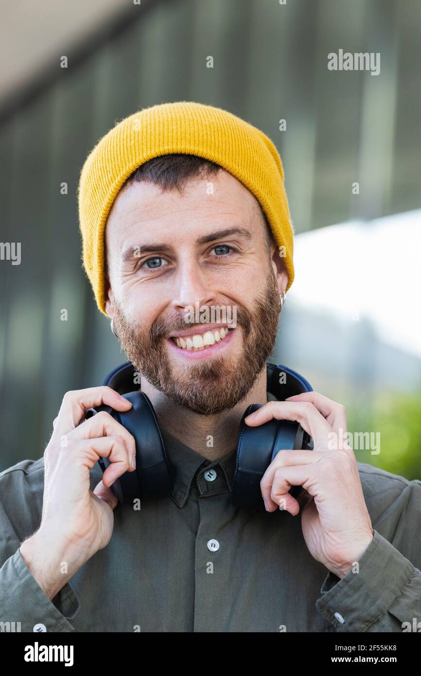 Smiling man holding headphones around neck against building Stock Photo