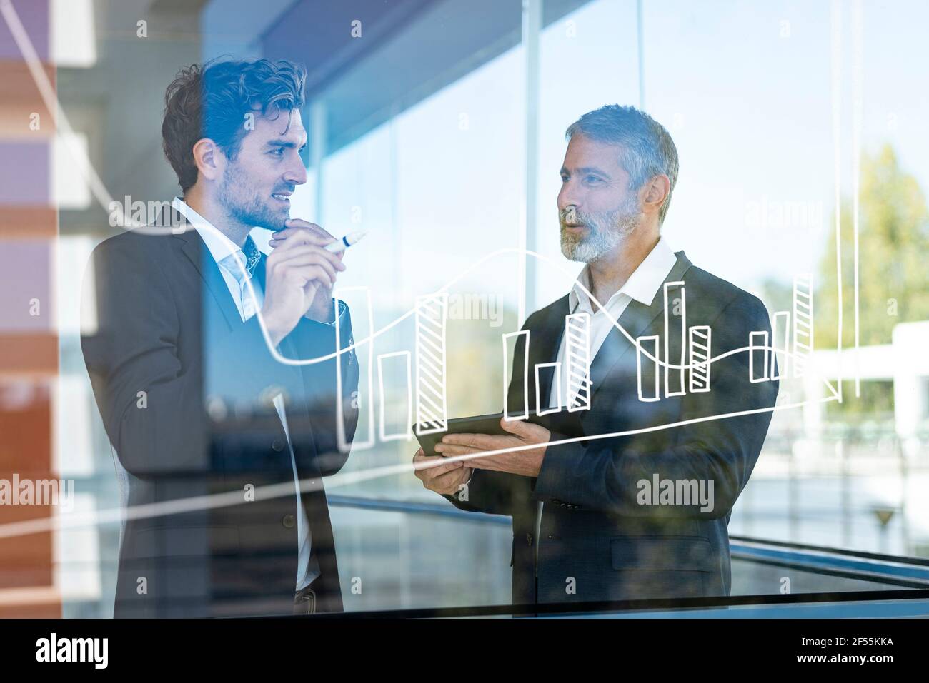 Businessmen discussing over graph while standing in modern office Stock Photo