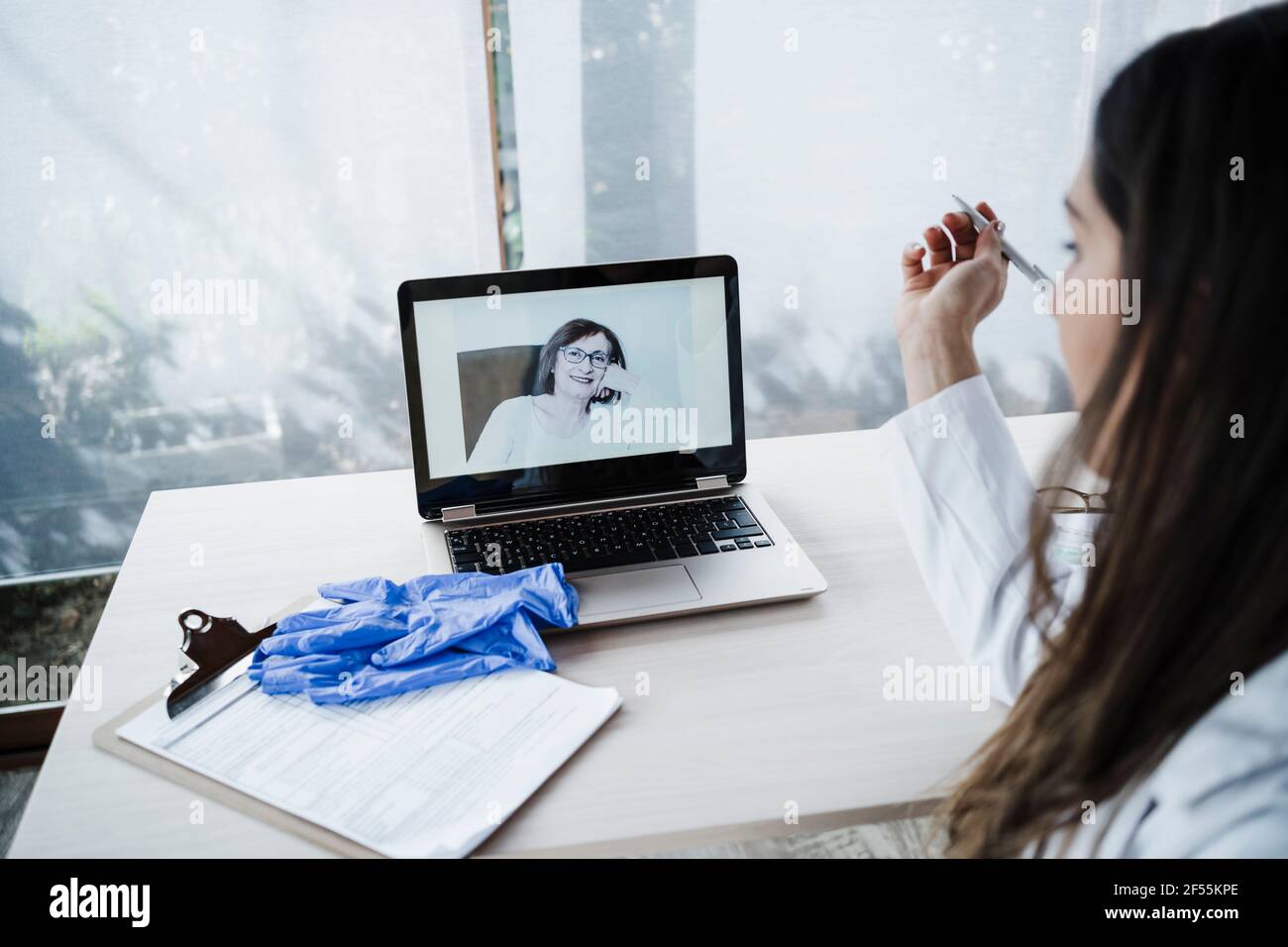 Female doctor teleassisting to senior patient through laptop at desk ...