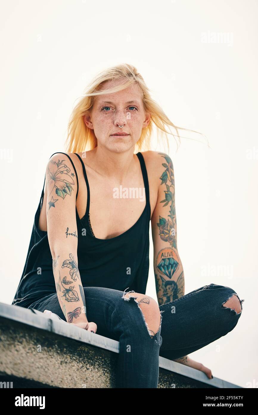 Tattooed young woman sitting on rooftop Stock Photo